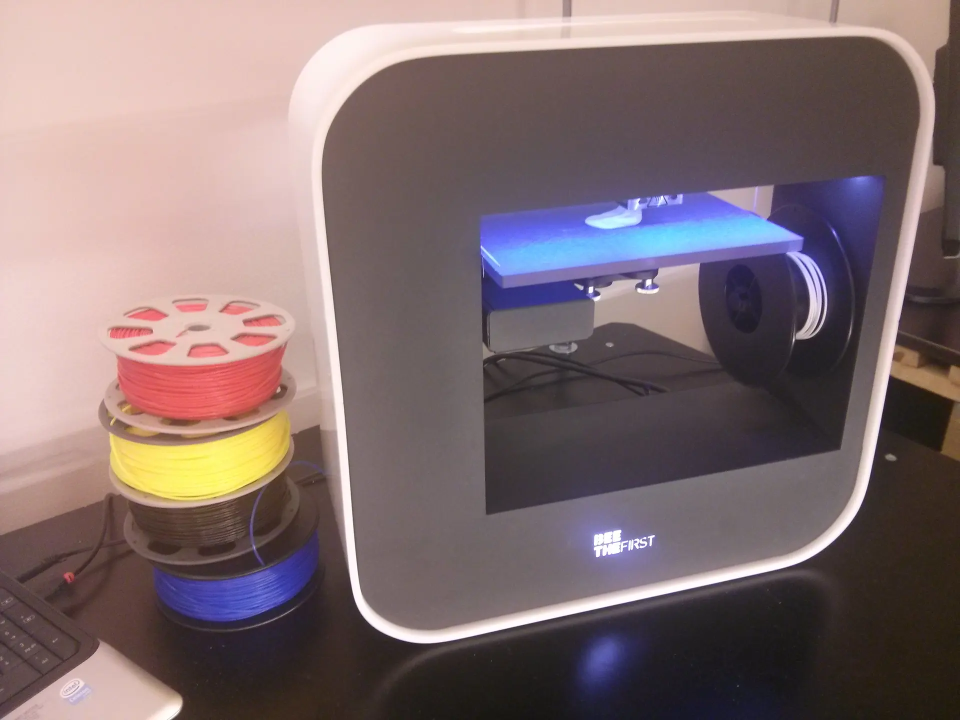 Spools of coloured filament beside a desktop 3D printer