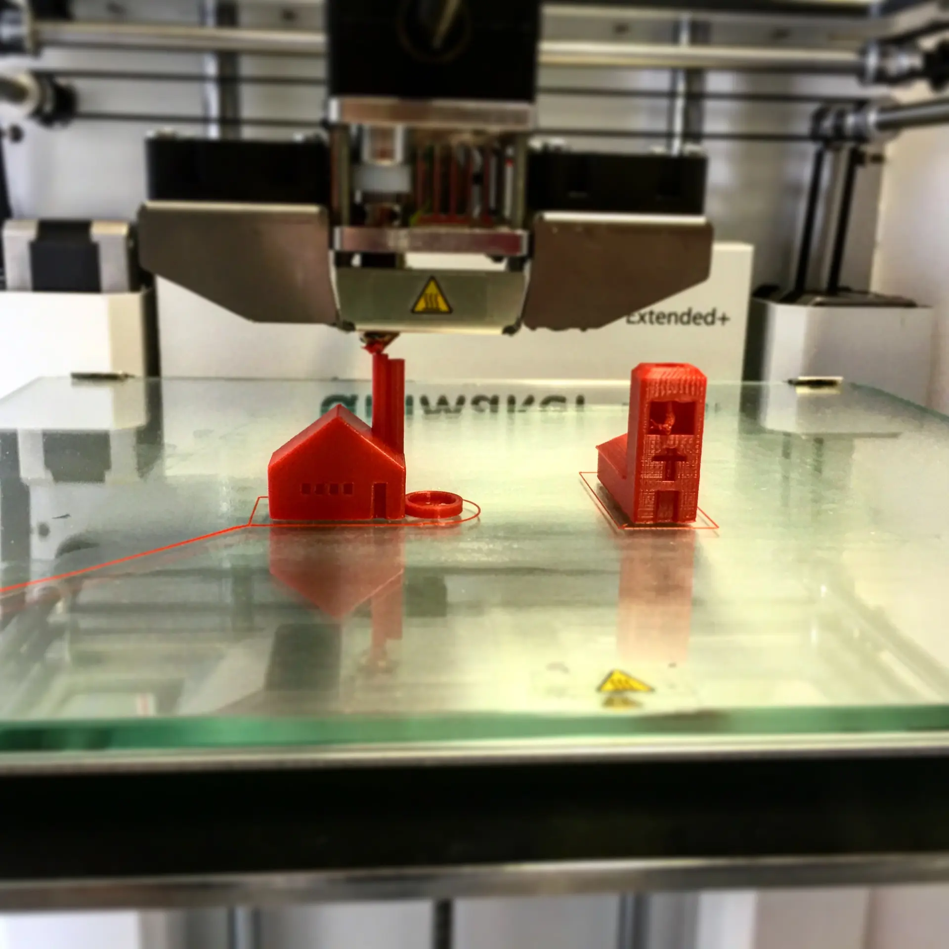 A 3D printer building small model houses on a glass bed